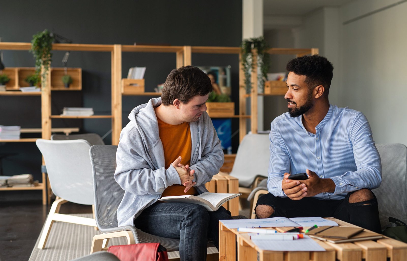 Young happy man with Autism and his tutor studying indoors at school.